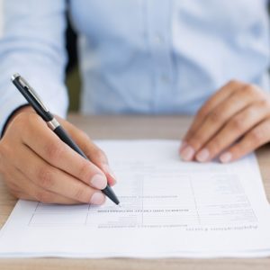 Cropped view of person holding pen and filling out application form on table